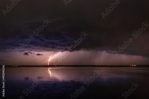 During a night thunderstorm, lightning from stormy clouds hits the ground, and reflected in the mirror surface of the lake