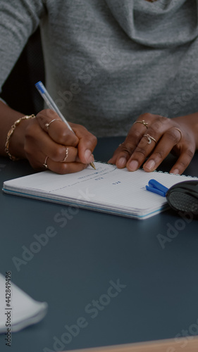 Closeup of student with black skin writing communication homework on notebook while sitting at desk in living room. Young woman studying math on elearning platform doing homework during high school photo