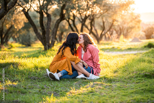 Two lesbian girls, sitting on the ground in a park, kissing each other on the mouth. lesbian concept