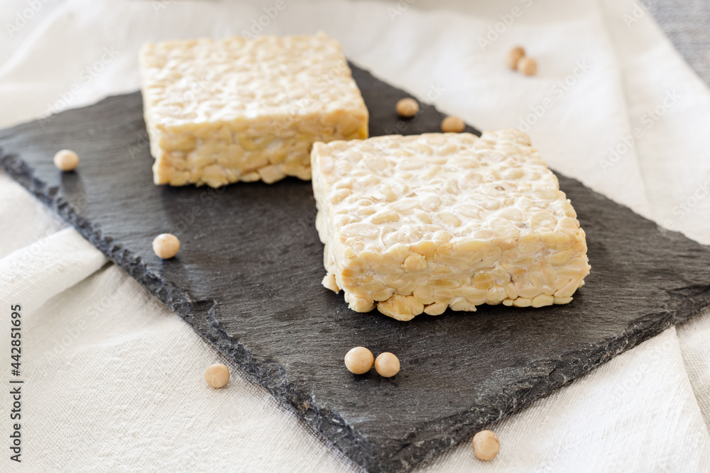 Tempeh natural on a black slate plate. Tempeh is a vegetable protein made from soybean-1
