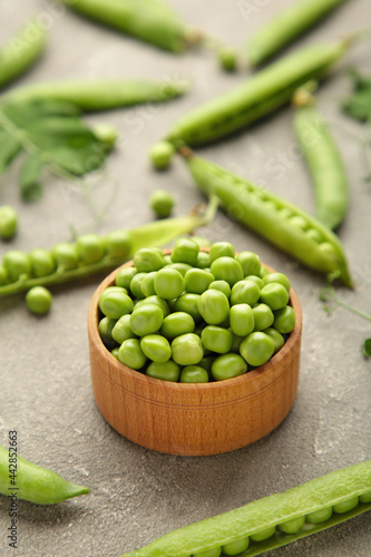 Green peas in wooden bowl on grey background