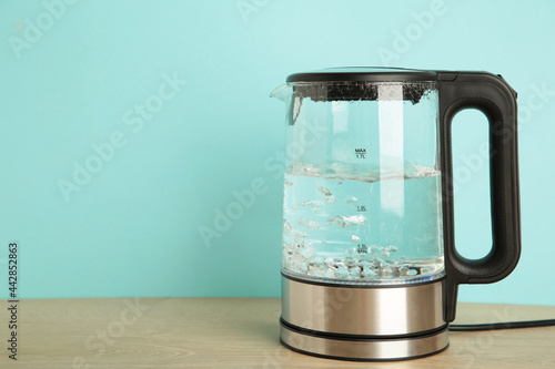 Glass electric kettle with boiling water on blue background. photo