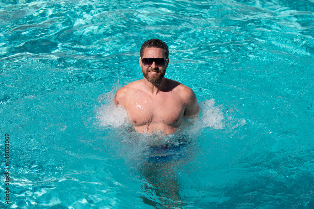 Handsome man in sunglasses swimming in pool. Summer resort. Summertime vacation.