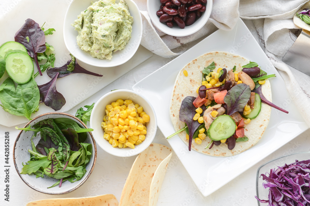 Composition with tacos, ingredients and tasty guacamole in bowl on light background Composition with tacos, ingredients and tasty guacamole in bowl on light background