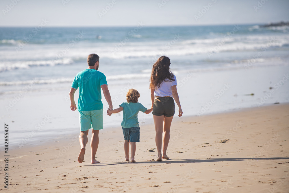 Back view of happy family on the beach. People having fun on summer vacation. Father, mother and child holding hands against blue sea. Holiday travel concept.
