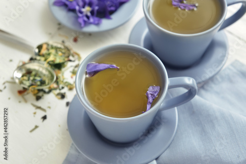 Cups with tasty floral tea on light wooden background