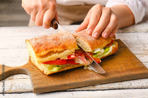 Woman cutting tasty sandwic...