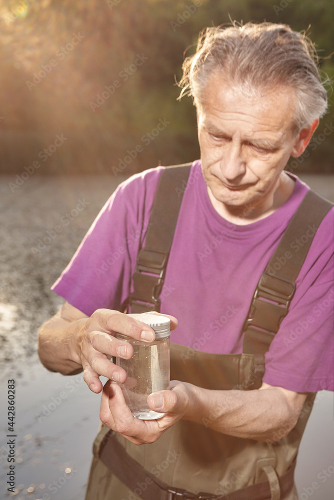 Water quality analyst dressed in chest wader closing bottle with water sample Water quality analyst dressed in chest wader closing bottle with water sample