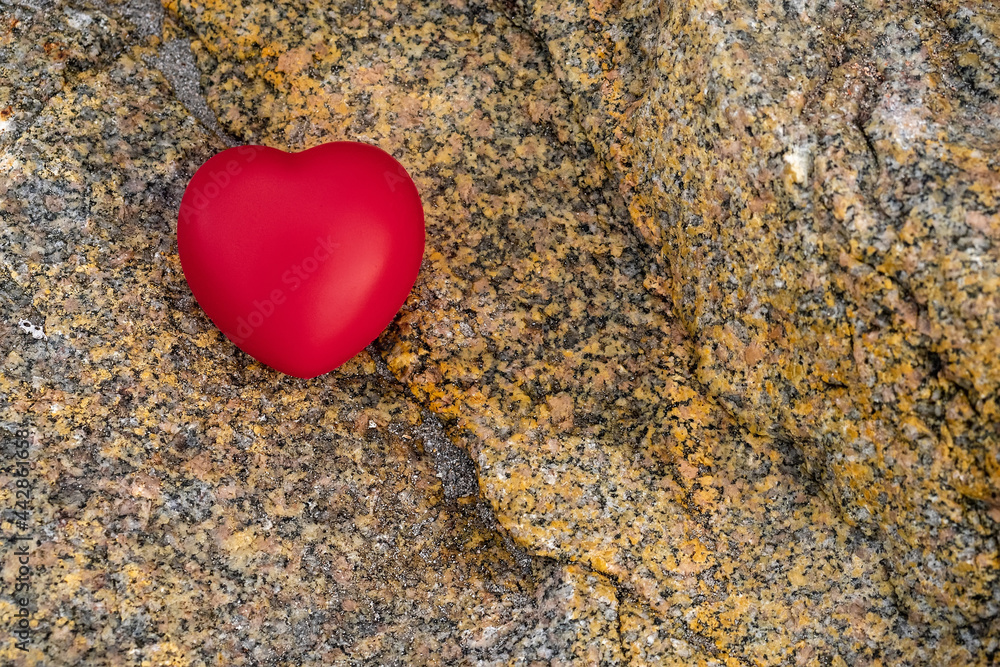 Fototapeta premium Red heart symbol of love on a rough stone surface. Abstract Saint Valentine background.
