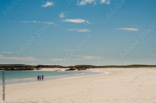 Three women enjoy magnificent Gurteen bay and beach  near Roundstone town  county Galway  Ireland  warm sunny day  cloudy sky. Beautiful Irish landscape  with clear water and light color sand