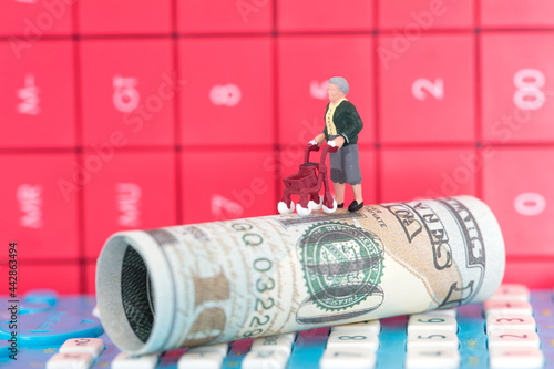 Lonely miniature old man model on dollar bills with calculator background behind