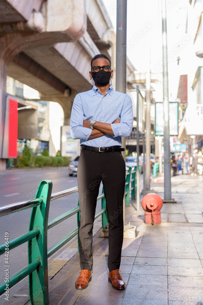 Full length shot of handsome black African businessman outdoors in city during summer wearing face mask