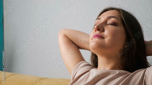Fotografija woman enjoying the wind from the fan while sitting on the couch, close-up