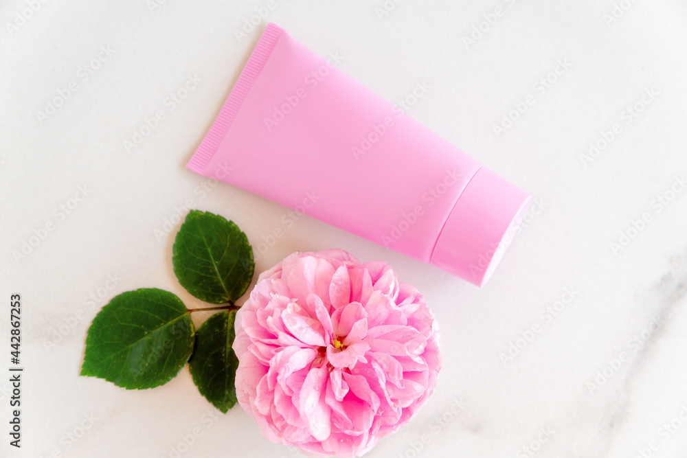 pink tube with rose face or body cream or scrub decorated with pink core flowers. Skin care concept. Unbranding mockup pink tube with rose face or body cream or scrub decorated with pink core flowers. Skin care concept. Unbranding mockup
