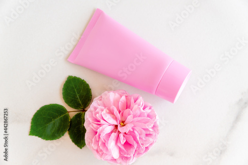 pink tube with rose face or body cream or scrub decorated with pink core flowers. Skin care concept. Unbranding mockup