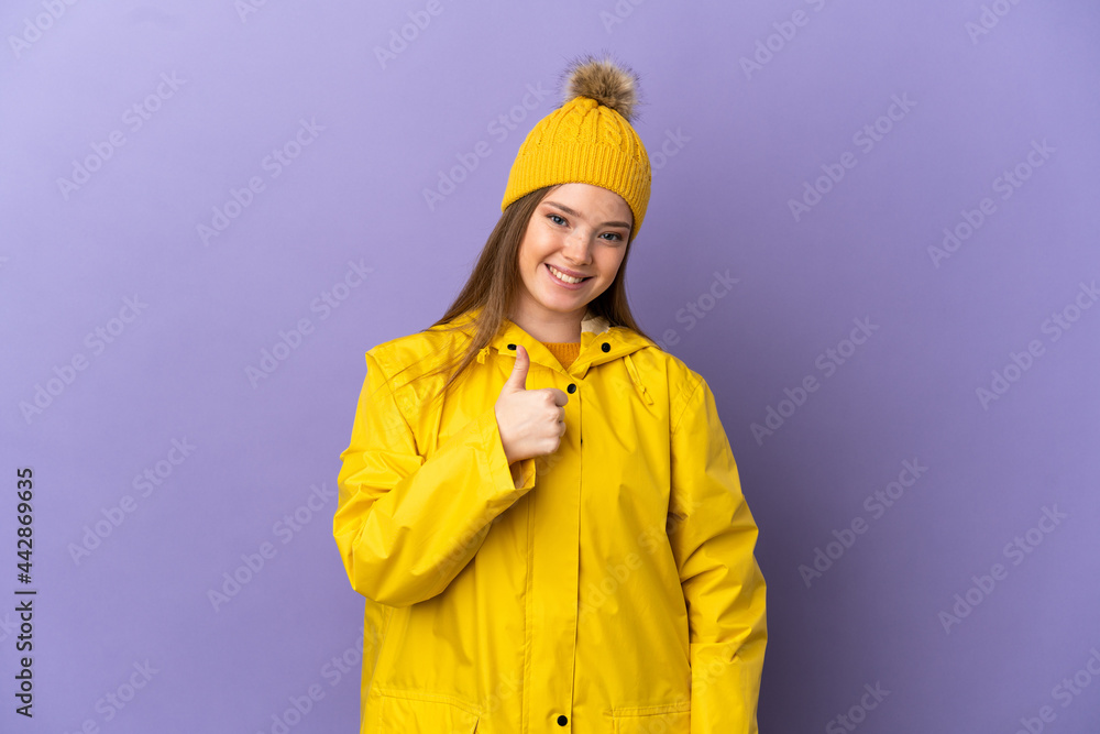 Teenager girl wearing a rainproof coat over isolated purple background giving a thumbs up gesture Teenager girl wearing a rainproof coat over isolated purple background giving a thumbs up gesture