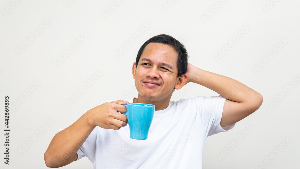A portrait of young Asian Malay man stress thinking about a problem, scratching head while holding a cup of tea on isolated white backgrounds. A portrait of young Asian Malay man stress thinking about a problem, scratching head while holding a cup of tea on isolated white backgrounds.