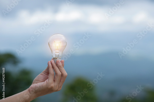 hand holding light bulb against nature, icons energy sources for renewable,