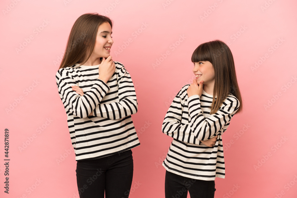 Little sisters girls isolated on pink background looking looking at each other Little sisters girls isolated on pink background looking looking at each other