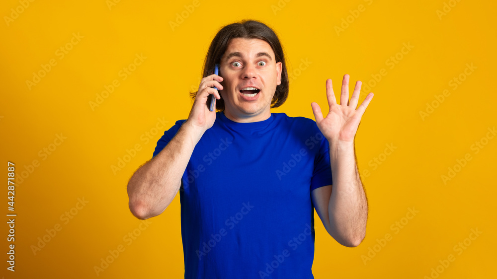 Banner. Emotional European man surprised talking mobile phone discusses something actively, wears t-shirt isolated over yellow background. Technology communication. Banner. Emotional European man surprised talking mobile phone discusses something actively, wears t-shirt isolated over yellow background. Technology communication.