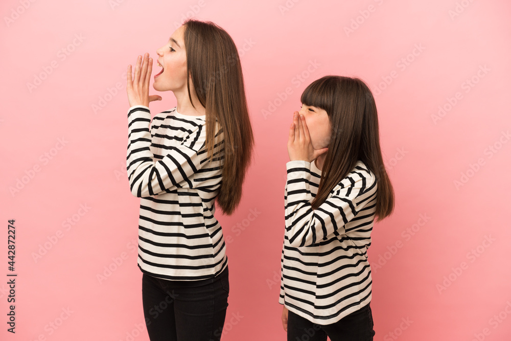Little sisters girls isolated on pink background shouting with mouth wide open to the lateral