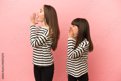 Little sisters girls isolated on pink background shouting with mouth wide open to the lateral