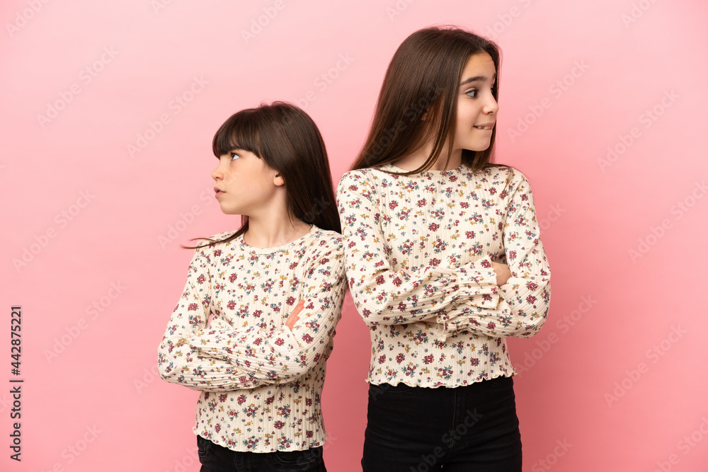 Little sisters girls isolated on pink background with confuse face expression while bites lip Little sisters girls isolated on pink background with confuse face expression while bites lip