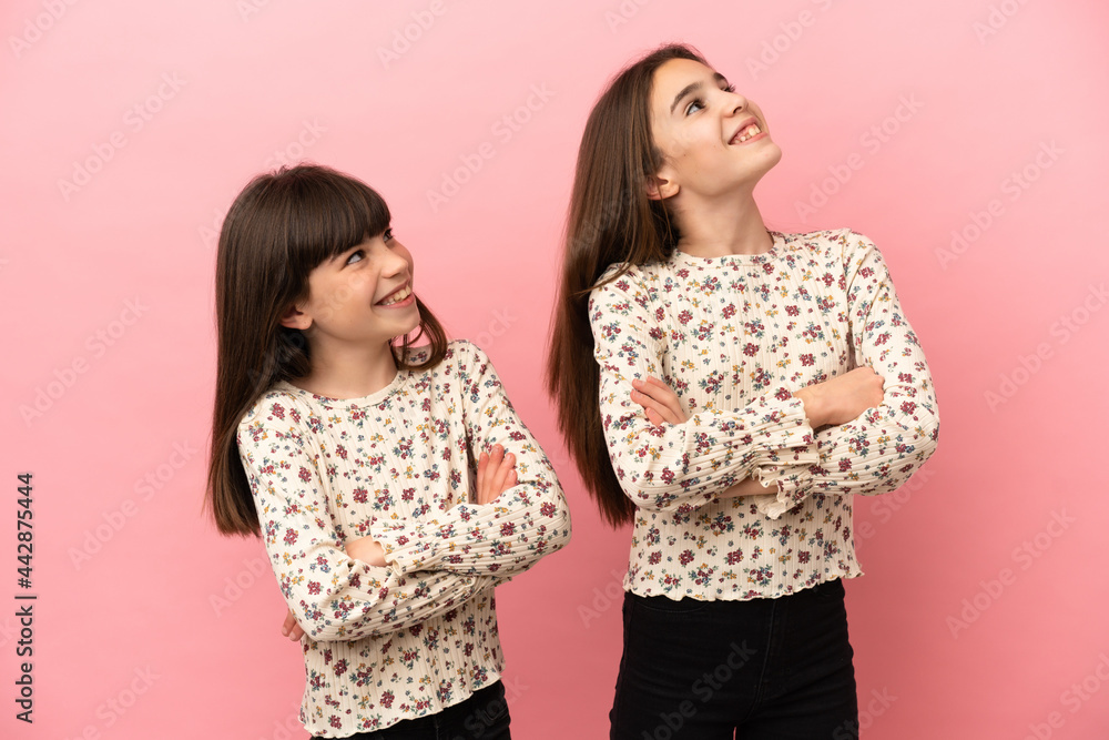 Little sisters girls isolated on pink background looking up while smiling Little sisters girls isolated on pink background looking up while smiling