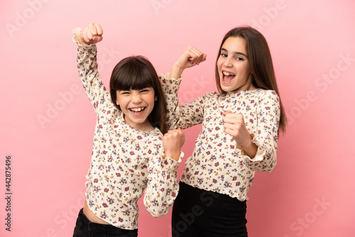 Little sisters girls isolated on pink background celebrating a victory