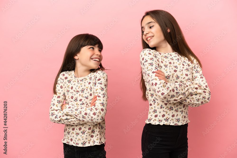 Little sisters girls isolated on pink background looking over the shoulder with a smile Little sisters girls isolated on pink background looking over the shoulder with a smile