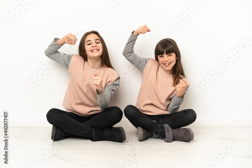 Little sisters sitting on the floor isolated on white background celebrating a victory