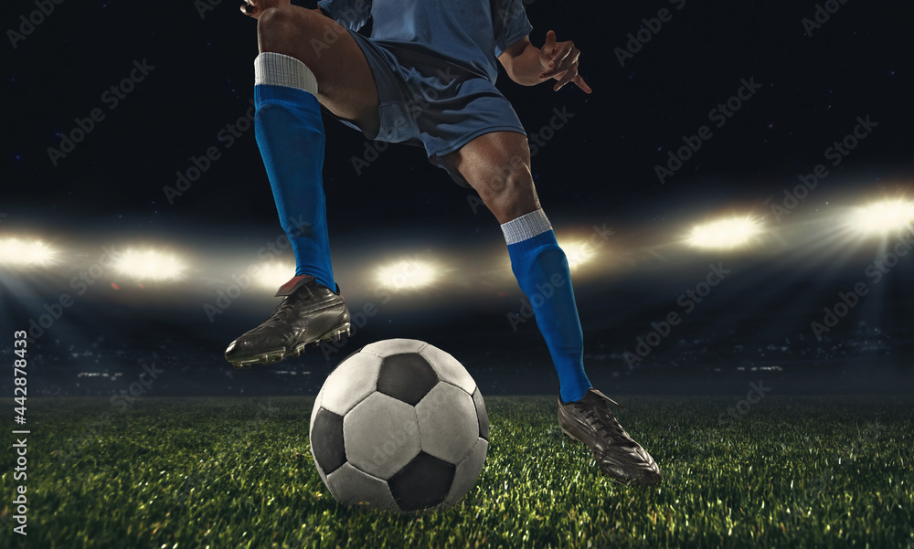 Cropped male soccer, football player kicking ball at the stadium during sport match on dark sky background.