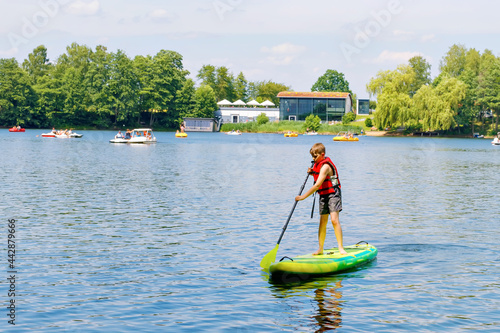 Kid boy paddling on sup board on a lake. Active child on modern trendy stand up paddle board. Summer outdoors vacations activity for family and children. Watersport activieties.