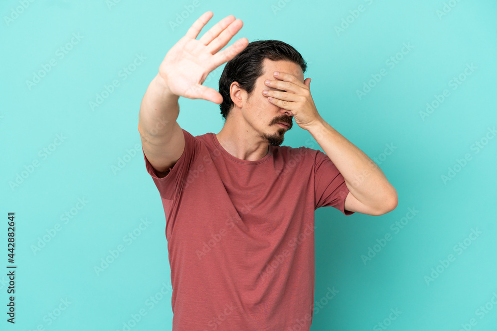 Young caucasian man isolated on blue background making stop gesture and covering face Young caucasian man isolated on blue background making stop gesture and covering face