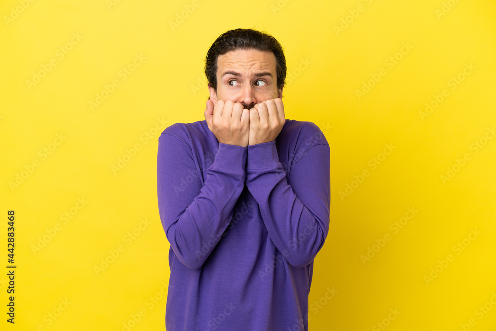Young caucasian man isolated on yellow background nervous and scared putting hands to mouth Young caucasian man isolated on yellow background nervous and scared putting hands to mouth