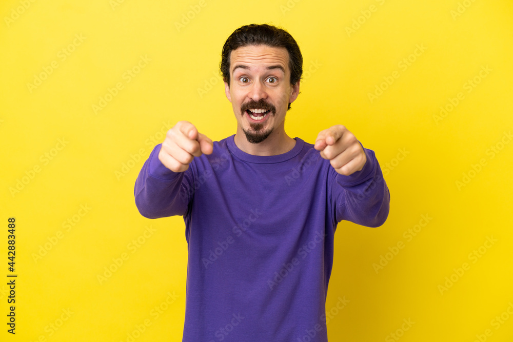 Young caucasian man isolated on yellow background surprised and pointing front Young caucasian man isolated on yellow background surprised and pointing front