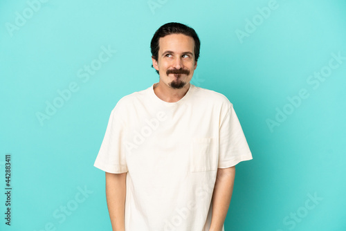 Young caucasian man isolated on blue background having doubts while looking up