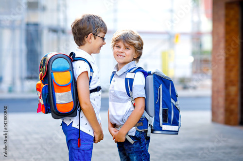 Two little kid boys with backpack or satchel. Schoolkids on the way to school. Healthy adorable children, brothers and best friends outdoors on the street leaving home. Back to school. Happy siblings. © Irina Schmidt