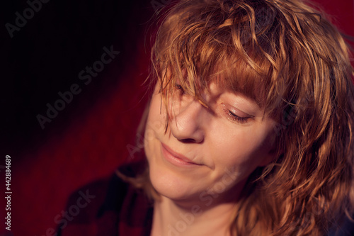 Portrait of smiling tousled disheveled middle-aged woman on red background. Unprofessional female model wiht smile posing in the Studio