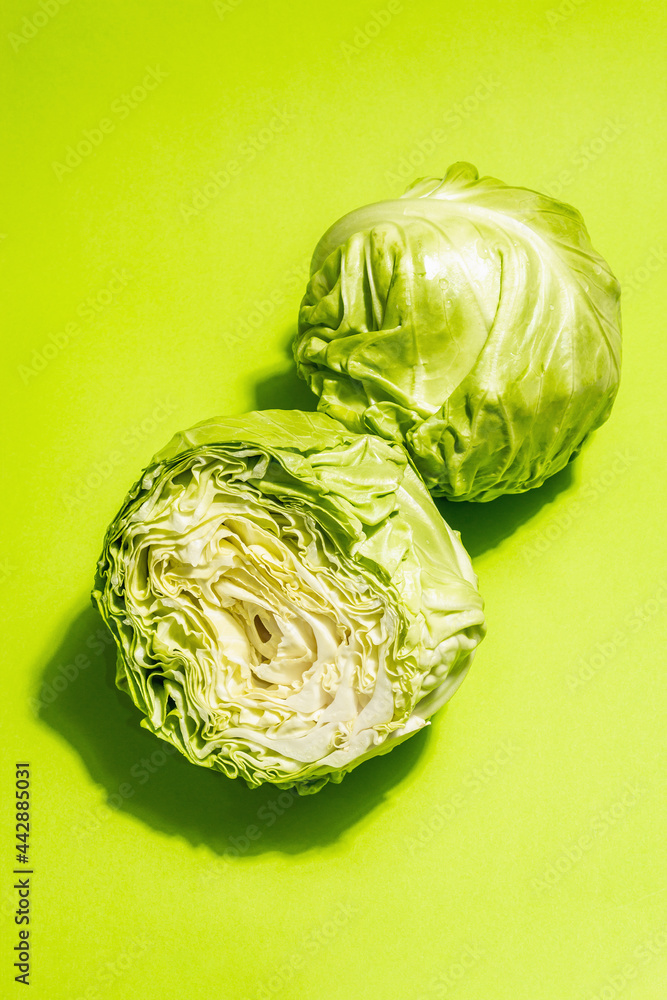 Obraz premium Fresh young cabbage, half and whole on bright green background