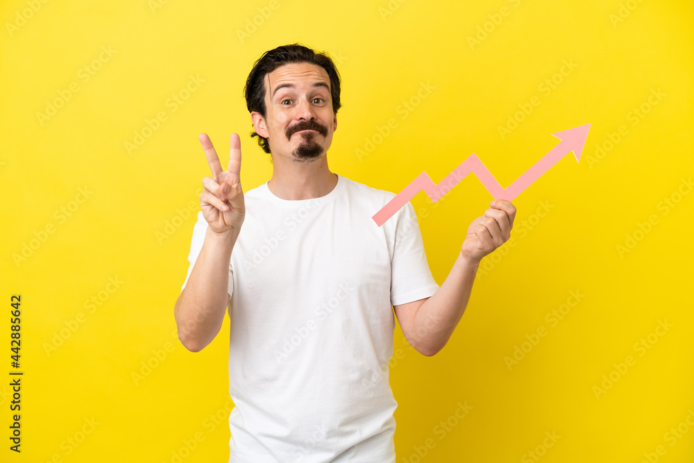 Young caucasian man isolated on yellow background holding a catching a rising arrow and celebrating a victory Young caucasian man isolated on yellow background holding a catching a rising arrow and celebrating a victory