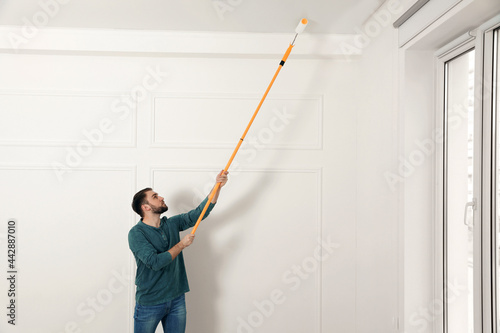 Young man painting ceiling with white dye indoors, space for text © New Africa