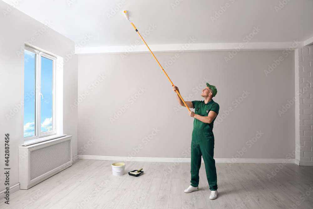 Man painting ceiling with roller in room Man painting ceiling with roller in room