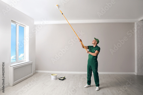 Man painting ceiling with roller in room © New Africa