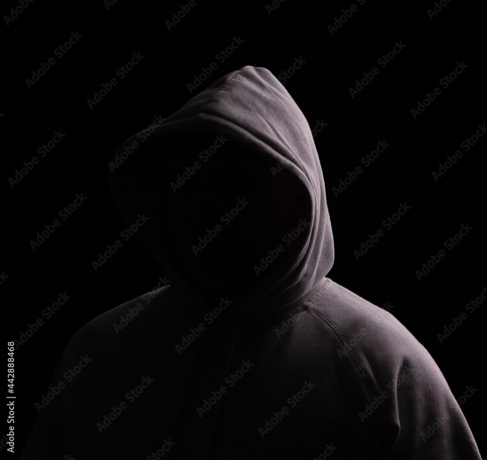 Hooded person with no face showing, just a dark area in that place, ideal for logo's and copy. Black background with moody lighting.