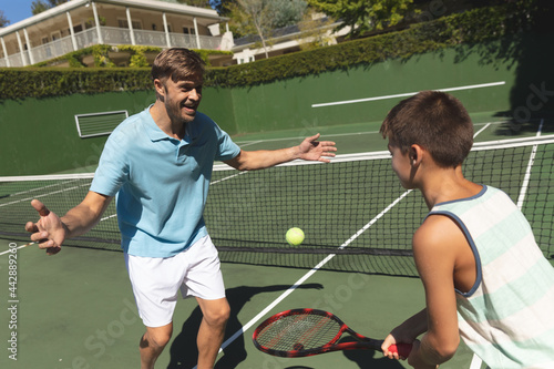 Happy caucasian father and son outdoors, playing tennis on tennis court