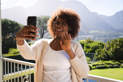 Happy african american woman on sunny balcony of country home making video call on smartphone