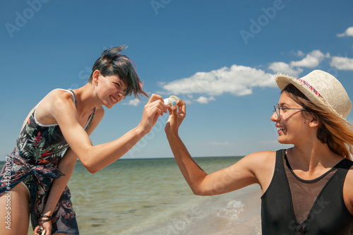 two women in swimsuits looking for a seashell on the seashore in the summer