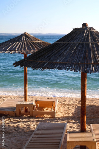 Fototapeta Naklejka Na Ścianę i Meble -  Bamboo parasol and wooden deck chair on a beautiful beach in Croatia.