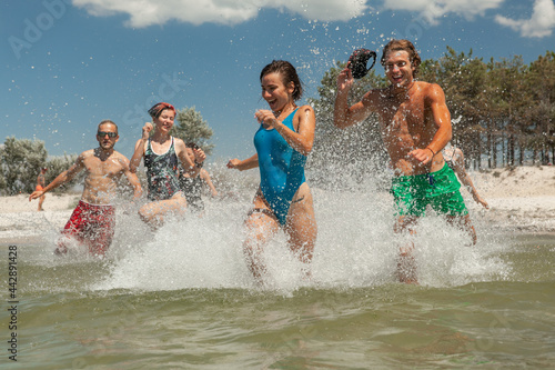 a group of friends consisting of men and women running on the beach in the sea